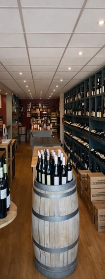 Cave à vin : sélection de bouteilles et fûts en bois Intérieur d'une cave à vin avec des bouteilles sur un tonneau en bois et des étagères remplies, ambiance chaleureuse.