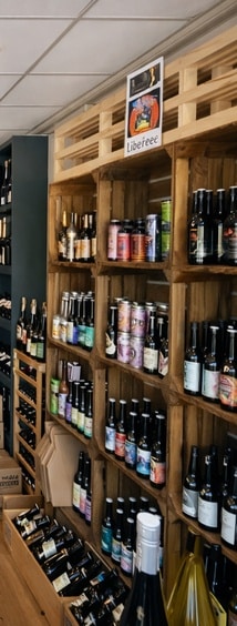 Cave à bières artisanales : sélection Libereee sur étagères Rayonnages en bois rustiques remplis de bouteilles de bières artisanales et canettes sous une affiche Libereee.