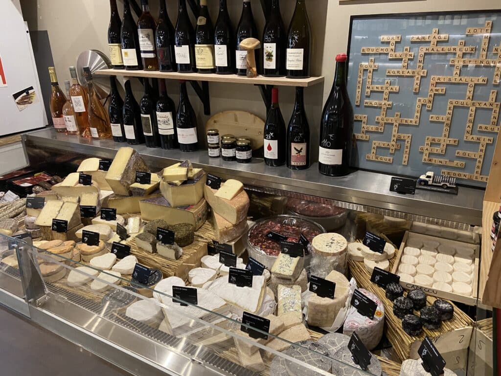 Fromagerie artisanale et cave : fromages affinés et vins Vitrine de fromagerie présentant divers fromages affinés, bouteilles de vin et décoration Scrabble thématique.