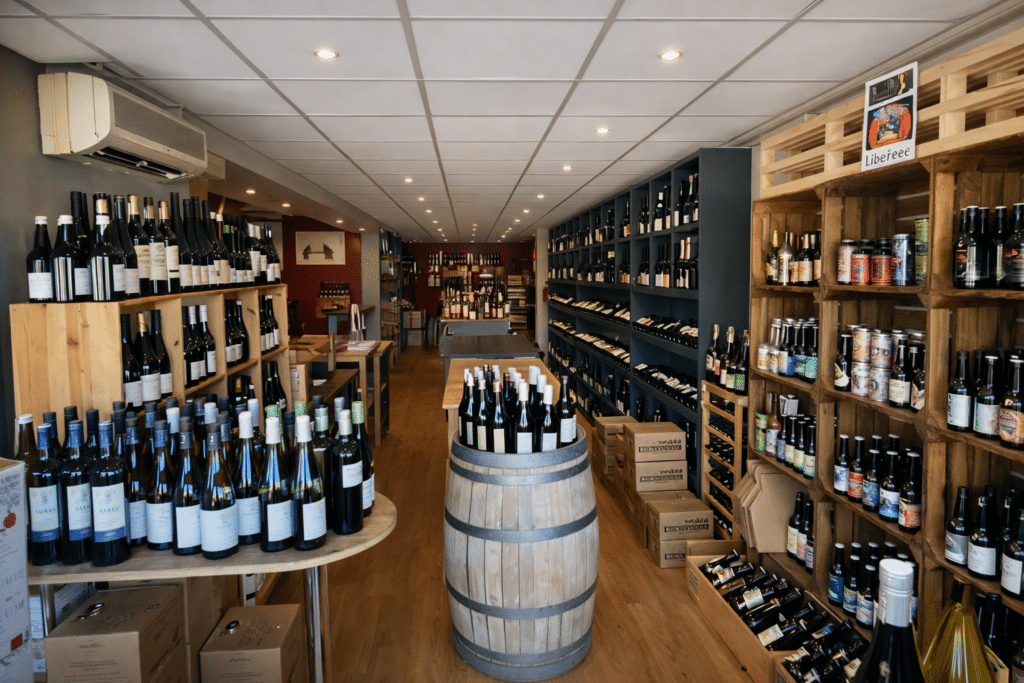 Intérieur d'une cave à vin avec bouteilles sur étagères en bois, tonneau central et affiche Libereee.