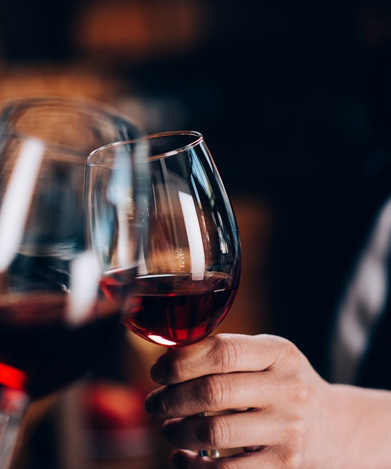 Vin rouge et toast entre amis dans une ambiance feutrée Deux verres de vin rouge levés pour un toast dans une ambiance tamisée, main tenant un verre à pied.
