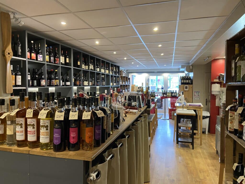 Intérieur de cave à vins avec liqueurs Jacoulot étiquetées sur comptoir en bois devant des étagères de bouteilles variées.