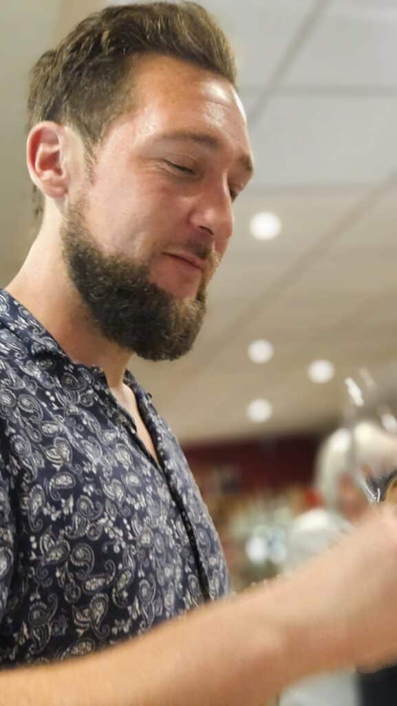 Homme barbu en chemise paisley : style et élégance Homme barbu aux cheveux bruns portant une chemise bleue à motifs paisley, regardant vers le bas avec sérénité.